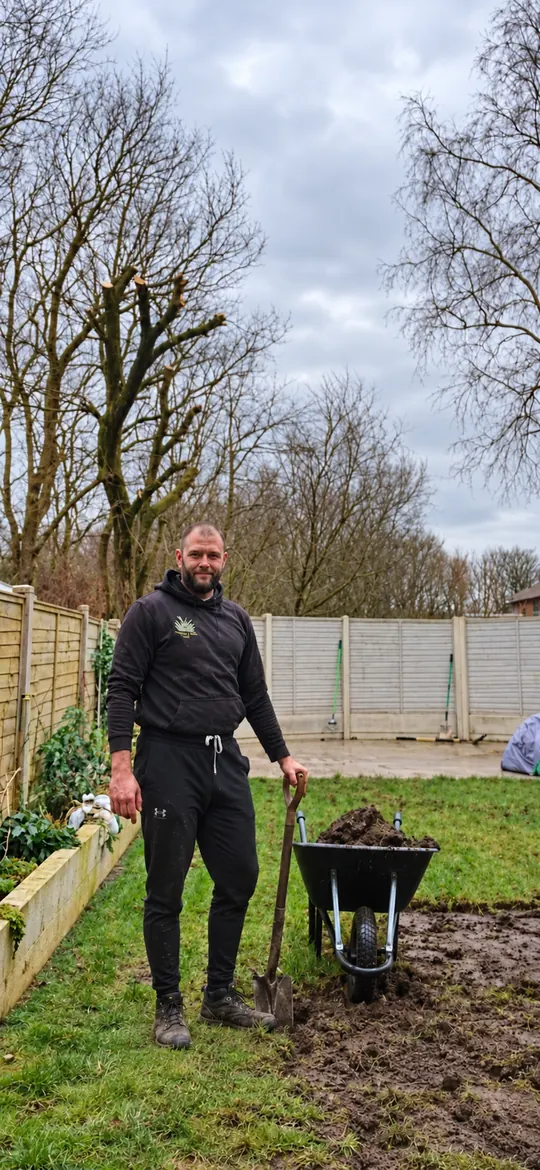 Gary Wilson, owner of G.W Artificial Grass LTD, preparing a garden with a spade and wheelbarrow