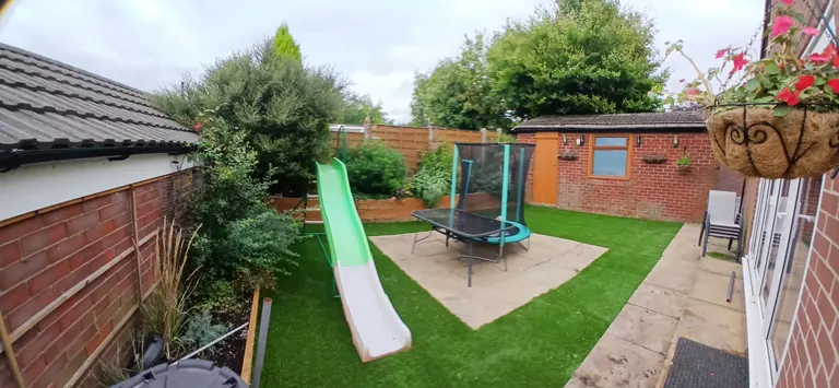 Artificial grass in a family garden with a slide and trampoline.