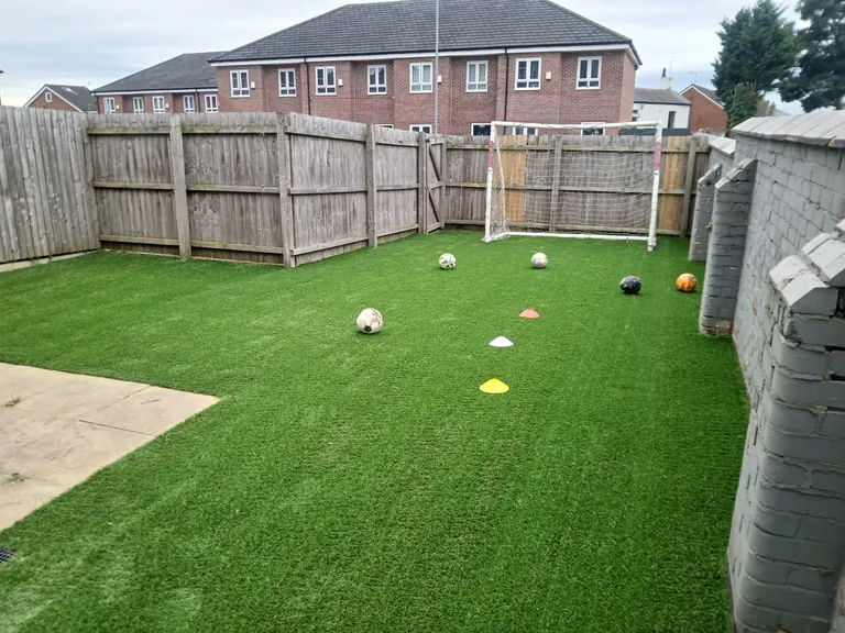 Artificial grass football practice space with a goal, balls and cones.