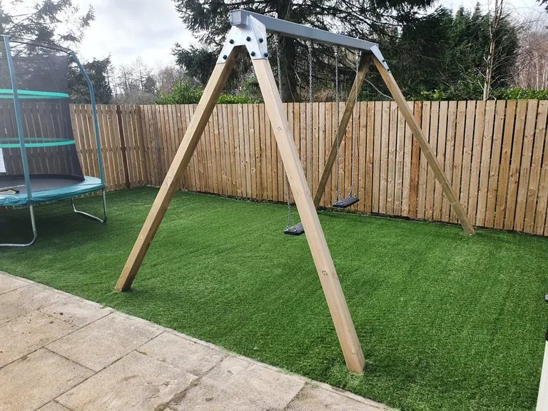 Artificial grass family play area around swings and a trampoline.